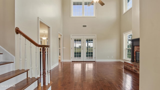 foyer with a fireplace, ceiling fan, a towering ceiling, and french doors