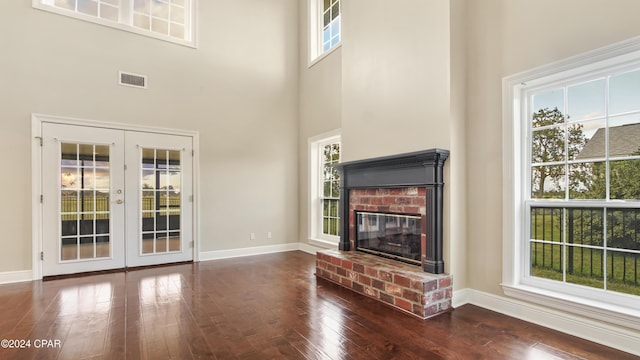 unfurnished living room with dark hardwood / wood-style floors, french doors, a towering ceiling, and a brick fireplace