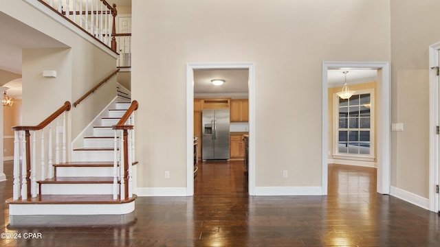 stairway with wood-type flooring, a notable chandelier, ornamental molding, and a towering ceiling