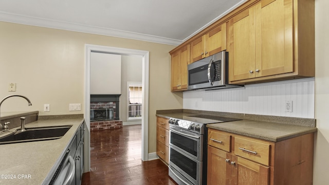 kitchen featuring dark wood-type flooring, stainless steel appliances, a fireplace, sink, and crown molding