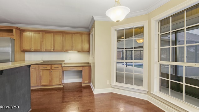 kitchen with built in desk, dark hardwood / wood-style flooring, hanging light fixtures, ornamental molding, and stainless steel refrigerator