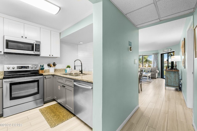 kitchen with white cabinetry, sink, light stone counters, a paneled ceiling, and appliances with stainless steel finishes