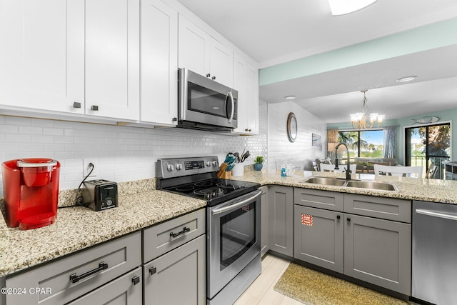 kitchen with gray cabinetry, sink, stainless steel appliances, a chandelier, and white cabinets