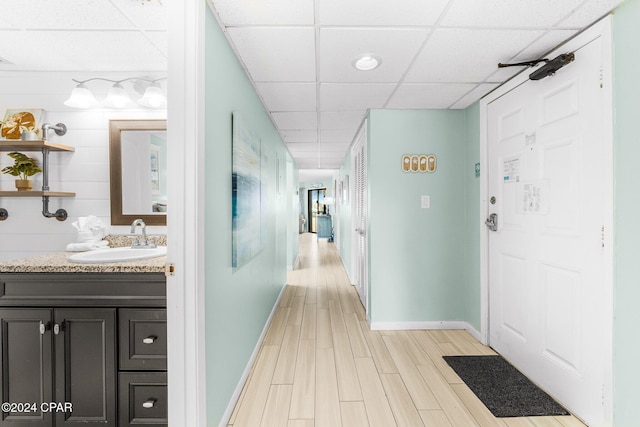 hallway with a drop ceiling, light wood-type flooring, and sink