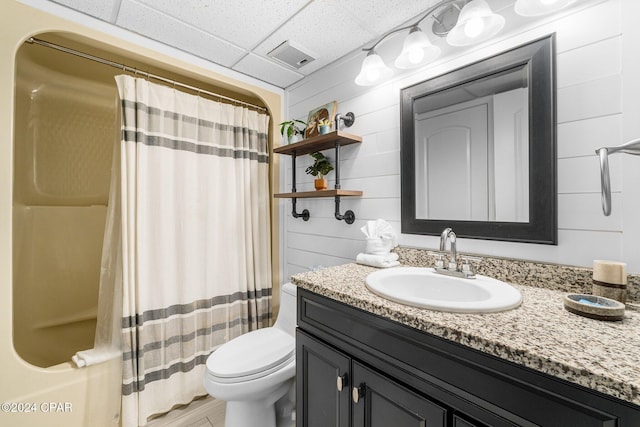 bathroom featuring a paneled ceiling, wooden walls, vanity, and toilet