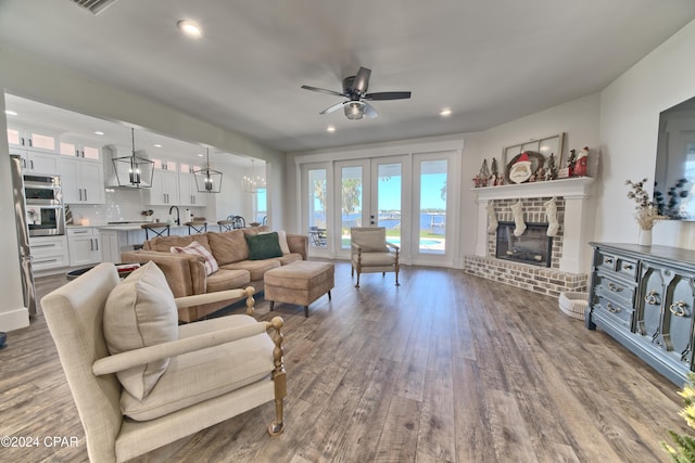 living room with french doors, a brick fireplace, ceiling fan with notable chandelier, sink, and hardwood / wood-style flooring