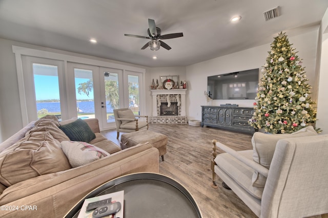 living room with hardwood / wood-style floors, french doors, a water view, a brick fireplace, and ceiling fan