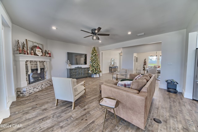 living room featuring a fireplace, wood-type flooring, and ceiling fan with notable chandelier