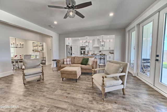 living room featuring ceiling fan with notable chandelier, light wood-type flooring, and french doors