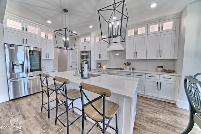 kitchen with white cabinets, stainless steel appliances, light hardwood / wood-style flooring, and a kitchen island with sink