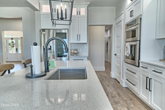 kitchen with light stone counters, white cabinets, hanging light fixtures, and light wood-type flooring