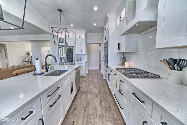 kitchen with pendant lighting, custom exhaust hood, appliances with stainless steel finishes, light hardwood / wood-style floors, and white cabinetry