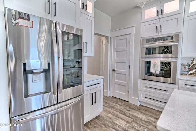 kitchen with light stone countertops, white cabinetry, light hardwood / wood-style flooring, and stainless steel appliances