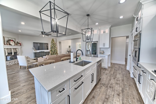 kitchen with sink, a kitchen island with sink, a fireplace, white cabinets, and light wood-type flooring