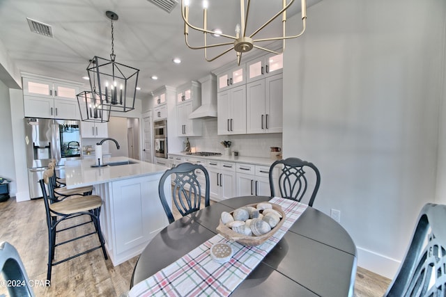 kitchen featuring appliances with stainless steel finishes, sink, decorative light fixtures, white cabinetry, and an island with sink