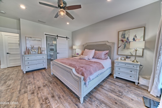 bedroom with a barn door, dark hardwood / wood-style floors, and ceiling fan