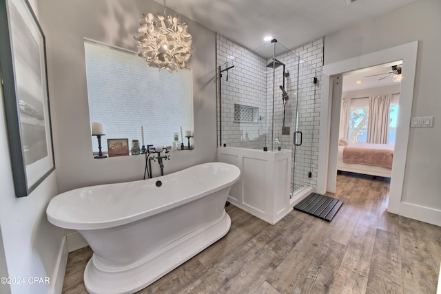 bathroom featuring plus walk in shower, wood-type flooring, and ceiling fan with notable chandelier