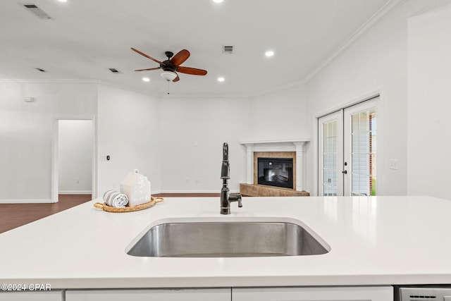 kitchen featuring hardwood / wood-style floors, sink, ceiling fan, ornamental molding, and a tiled fireplace