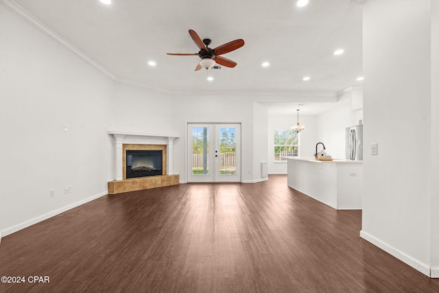 unfurnished living room with a tile fireplace, french doors, dark wood-type flooring, crown molding, and ceiling fan with notable chandelier