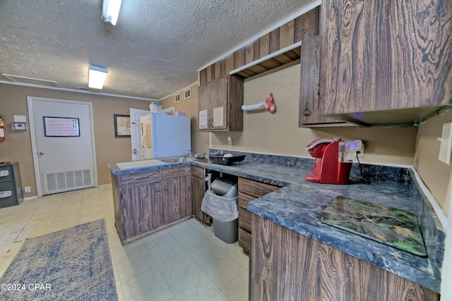 kitchen with a textured ceiling, white refrigerator, and sink