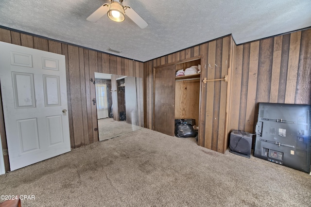 interior space with carpet flooring, ceiling fan, wood walls, and a textured ceiling