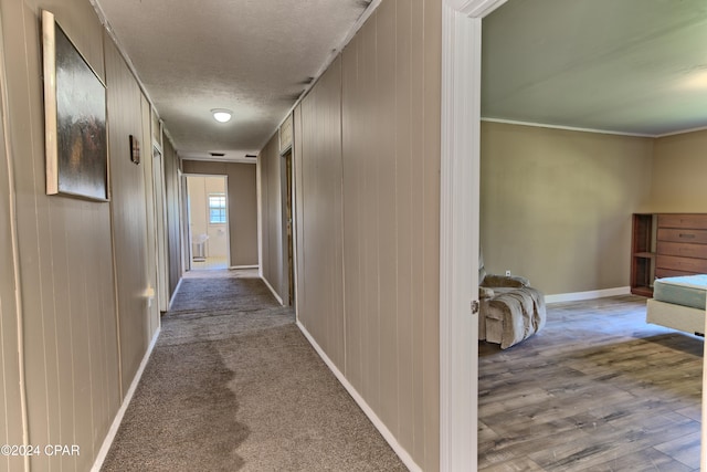 corridor featuring a textured ceiling, light hardwood / wood-style floors, wood walls, and crown molding