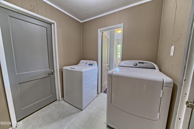 clothes washing area with a textured ceiling, washer and clothes dryer, crown molding, and wood walls