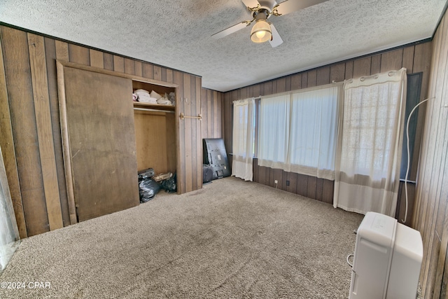 unfurnished bedroom with a textured ceiling, carpet floors, ceiling fan, and wood walls