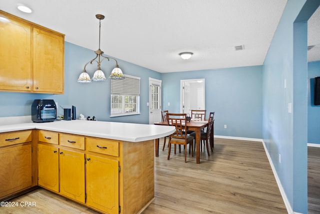 kitchen with decorative light fixtures, light hardwood / wood-style floors, and kitchen peninsula