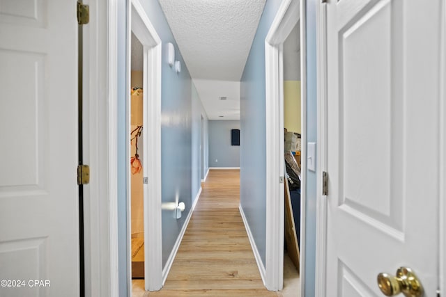 hallway with a textured ceiling and light hardwood / wood-style floors