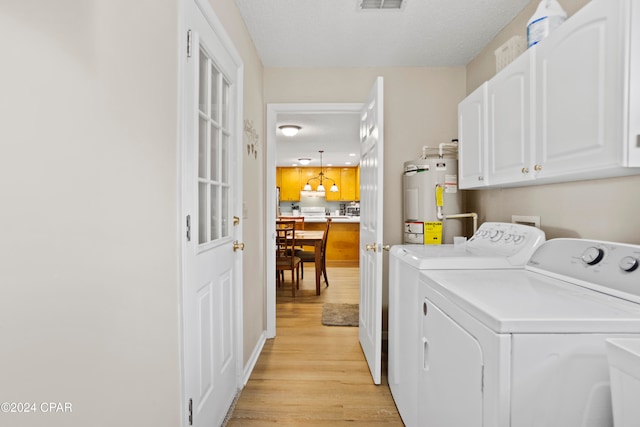 washroom with cabinets, a textured ceiling, electric water heater, light hardwood / wood-style flooring, and washing machine and dryer