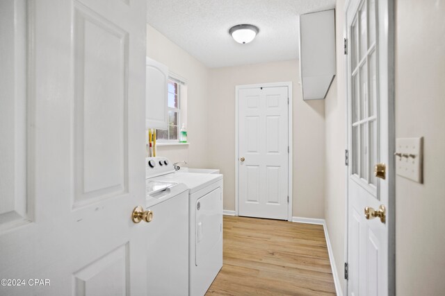 laundry room featuring washer and dryer, a textured ceiling, and light hardwood / wood-style flooring