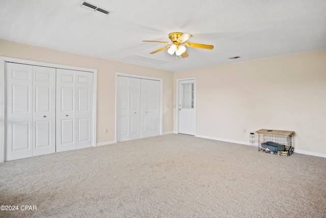 unfurnished bedroom featuring a textured ceiling, ceiling fan, carpet, and two closets