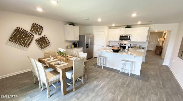 kitchen featuring white cabinetry, hardwood / wood-style floors, an island with sink, a breakfast bar, and appliances with stainless steel finishes