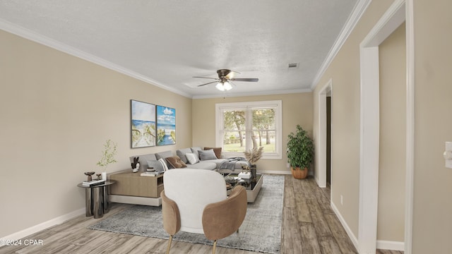 living room featuring ceiling fan, crown molding, light wood-type flooring, and a textured ceiling