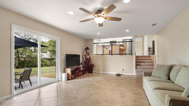 tiled living room with built in features, a stone fireplace, and ceiling fan