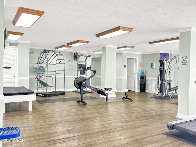 exercise room featuring crown molding, a textured ceiling, visible vents, and wood finished floors