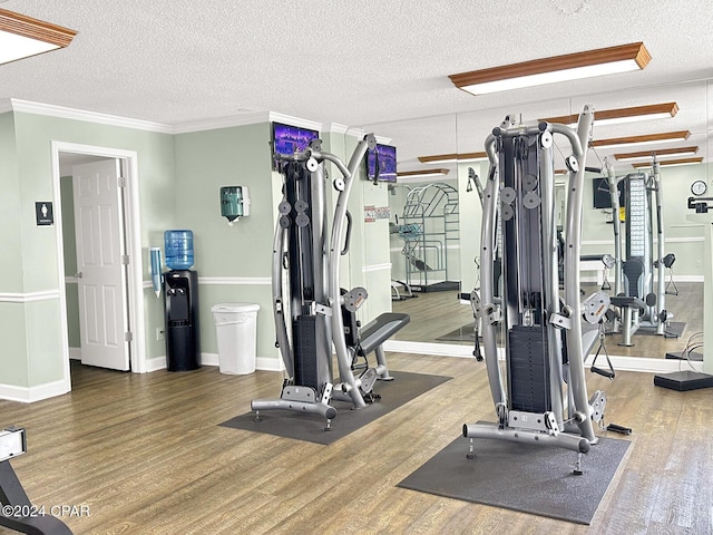 exercise room featuring crown molding, a textured ceiling, baseboards, and wood finished floors