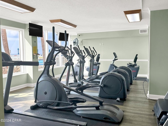 exercise room featuring hardwood / wood-style floors, a textured ceiling, and ornamental molding