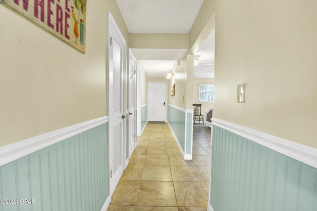 hall with light tile patterned flooring, a textured ceiling, and wainscoting