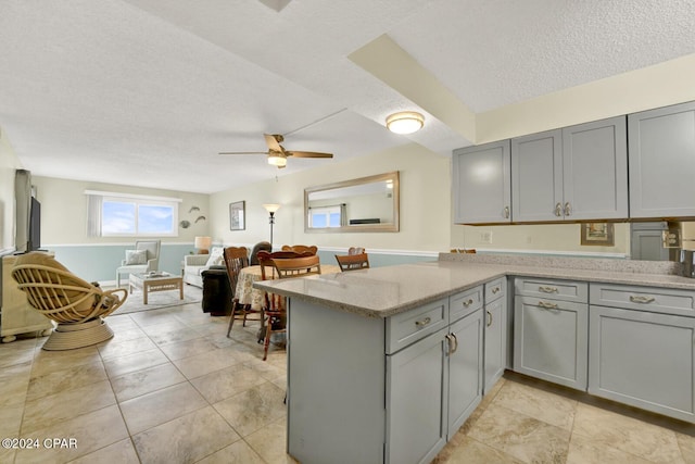 kitchen featuring light stone counters, a peninsula, gray cabinetry, and a textured ceiling