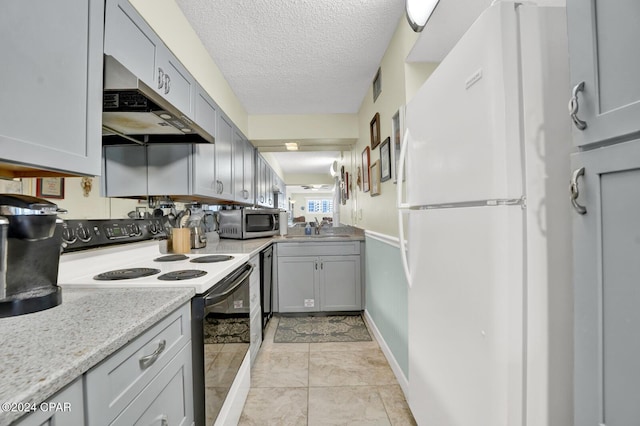 kitchen with stainless steel microwave, electric range, freestanding refrigerator, a textured ceiling, and under cabinet range hood