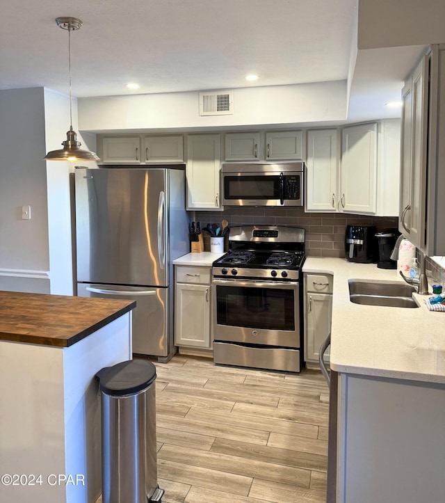 kitchen with appliances with stainless steel finishes, gray cabinetry, decorative backsplash, hanging light fixtures, and sink