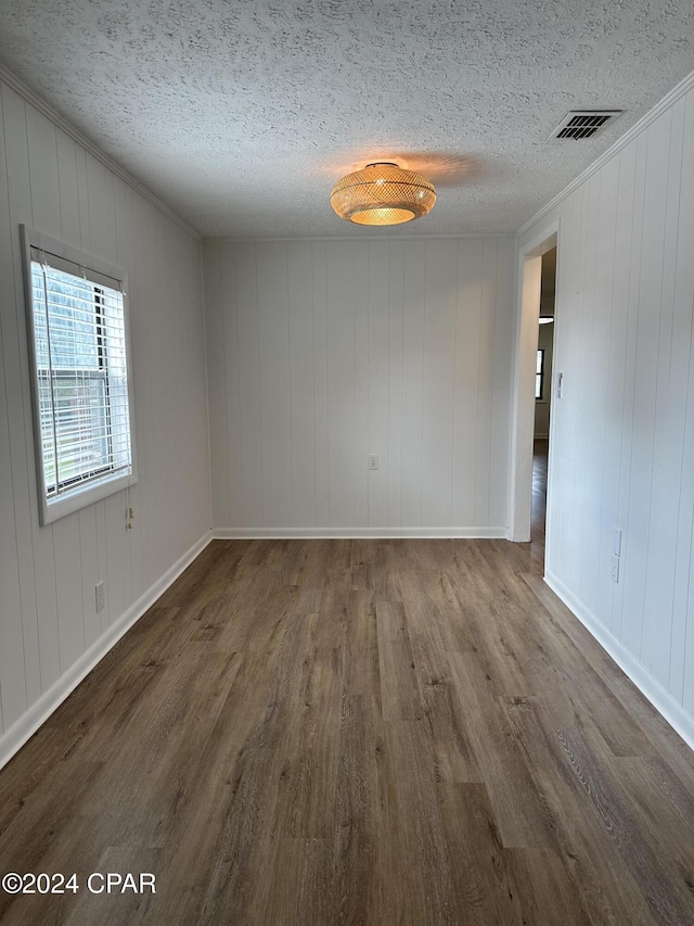 unfurnished room with ornamental molding, a textured ceiling, dark wood-type flooring, and wood walls