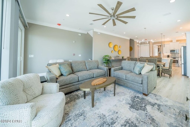 living room featuring ceiling fan, ornamental molding, and light wood-type flooring