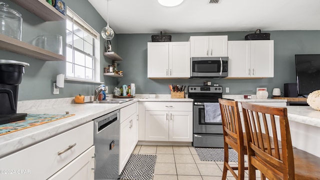 kitchen with stainless steel appliances, white cabinetry, light tile patterned floors, and decorative light fixtures