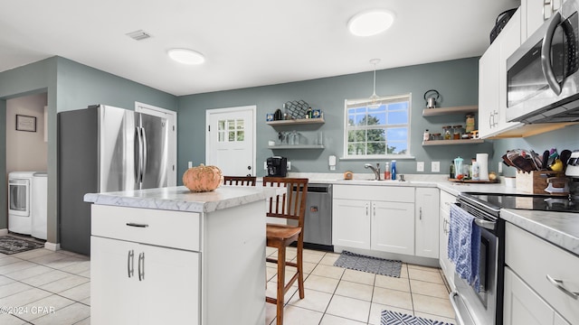 kitchen with light tile patterned floors, hanging light fixtures, stainless steel appliances, white cabinets, and washer / clothes dryer