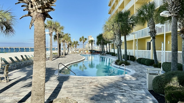 community pool with a water view, a patio area, and fence