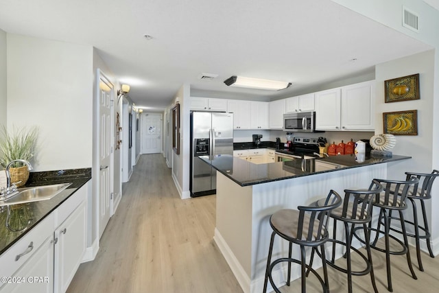 kitchen with a peninsula, appliances with stainless steel finishes, a sink, and white cabinets