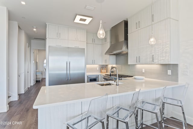 kitchen with pendant lighting, kitchen peninsula, wall chimney range hood, and stainless steel appliances